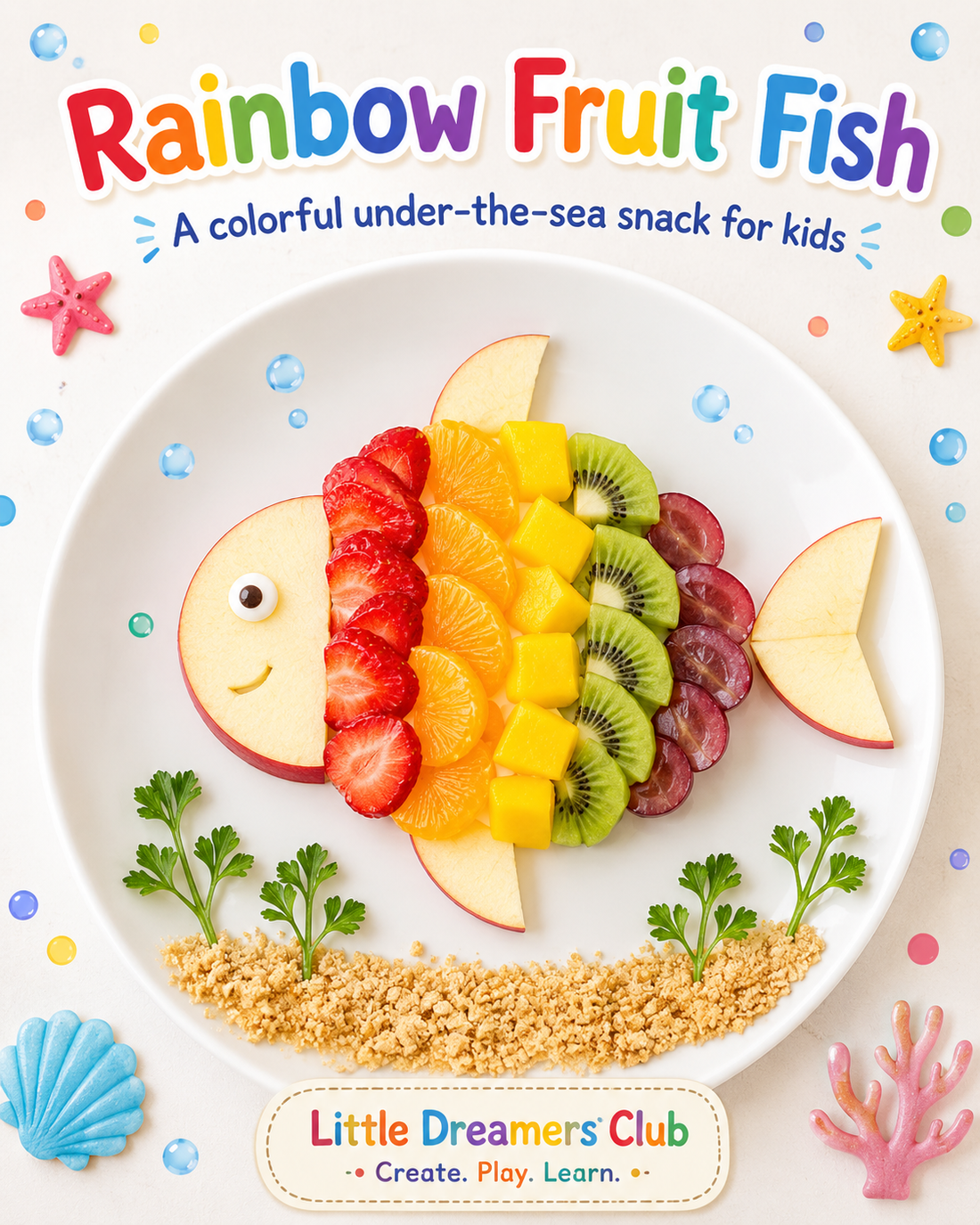 Rainbow fruit fish snack made with apple slices, strawberries, mango, kiwi, grapes, and graham cracker sand on a white plate for kids’ ocean food art.