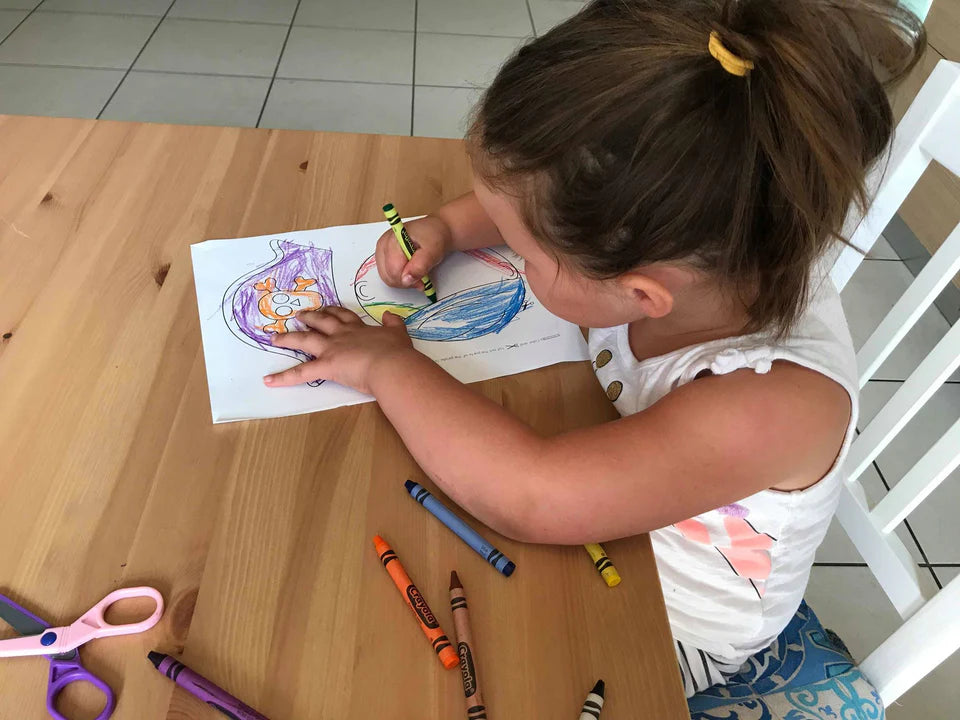 Child coloring at a table with crayons and scissors