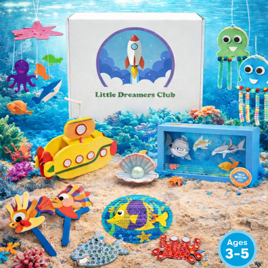 Little Dreamers Club Ages 3–5 ocean-themed craft box displayed on a sandy underwater backdrop, featuring a white box with the Little Dreamers Club logo surrounded by colorful sea-life crafts including jellyfish hangers, fish puppets, a yellow submarine, a shark diorama, a pearl shell, and crab and dolphin projects.