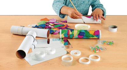 Child making a craft project with paper rolls and colorful decorations on a wooden table.