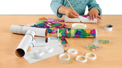 Child making a craft project with paper rolls and colorful decorations on a wooden table.