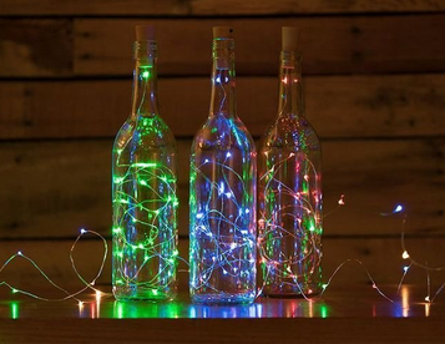 Three plastic wine bottles with string lights on a wooden surface