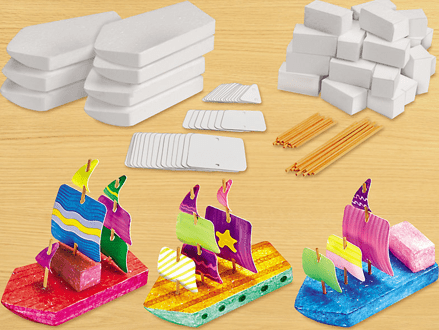 Colorful model sailboats made from foam with building blocks and sticks on a wooden surface.