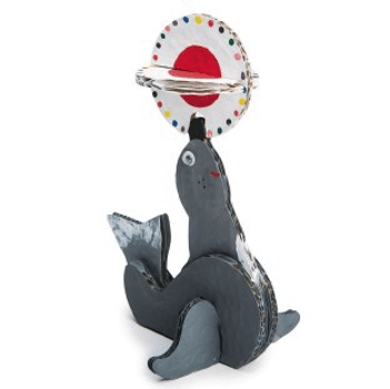 Gray cardboard seal balancing a ball on his nose on a white background.